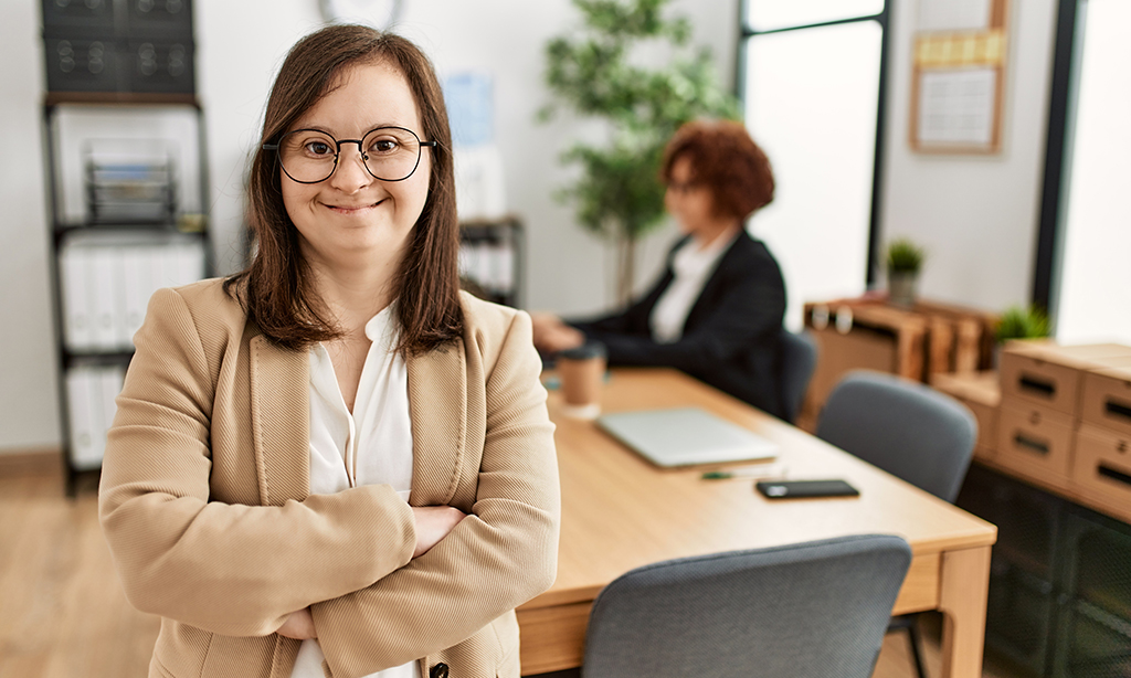 Eine junge Frau mit Downsyndrom steht in einem Großraumbüro.