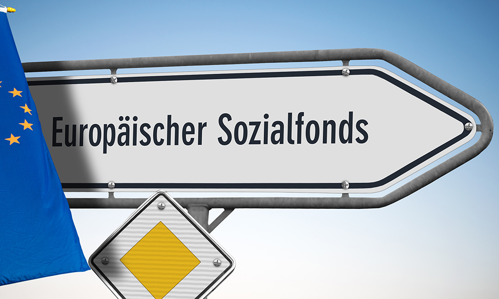 Wegweiser mit der Aufschrift „Europäischer Sozialfonds“, ein Vorfahrtsschild sowie eine Europäische Flagge