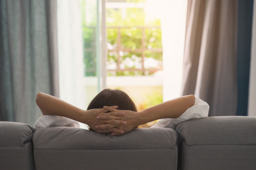 Eine Frau sitzt mit hinter dem Kopf verschränkten Armen auf einem Sofa.
