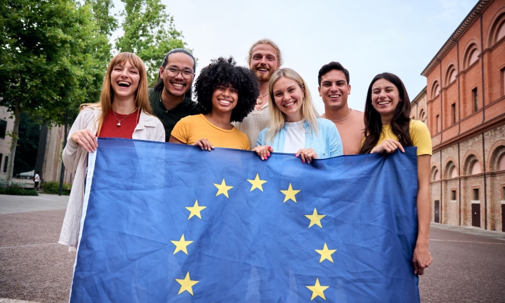 Eine multikulturelle Gruppe von jungen Leuten hält stolz die Flagge der Europäischen Union hoch.