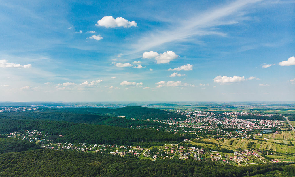 Luftaufnahme von einer Stadt, die an einen größeren Wald und Felder grenzt. 